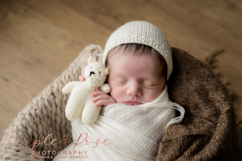 Newborn baby sleeping holding a cream teddy bear