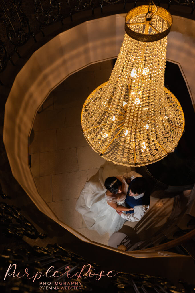Photo of bride and groom stood under a chandalier on their wedding day in Milton Keynes