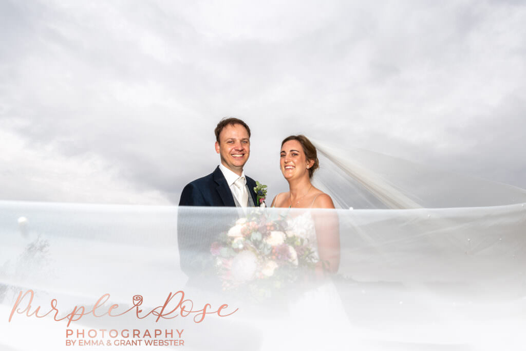 Photo of a bride and groom on their wedding day, with brides veil swirling around them on their wedding day in Milton Keynes