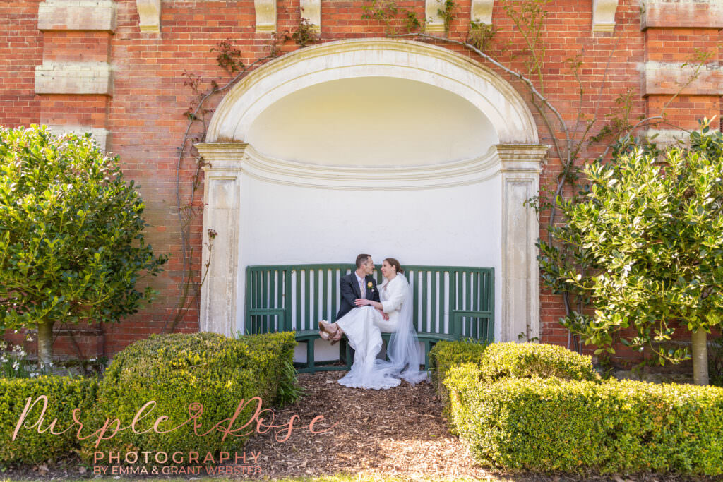 Photograph of a bride and groom sat in an alcove in the garden at their wedding venue in Milton Keynes