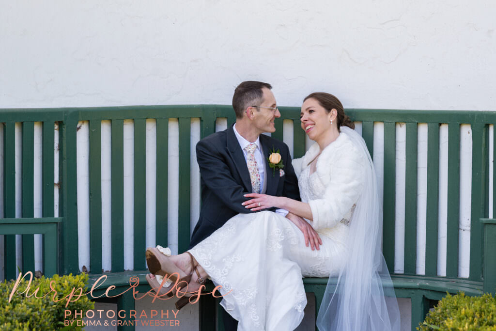 Photo of a bride and groom sat on a bench in the garden of their wedding venue in Milton Keynes