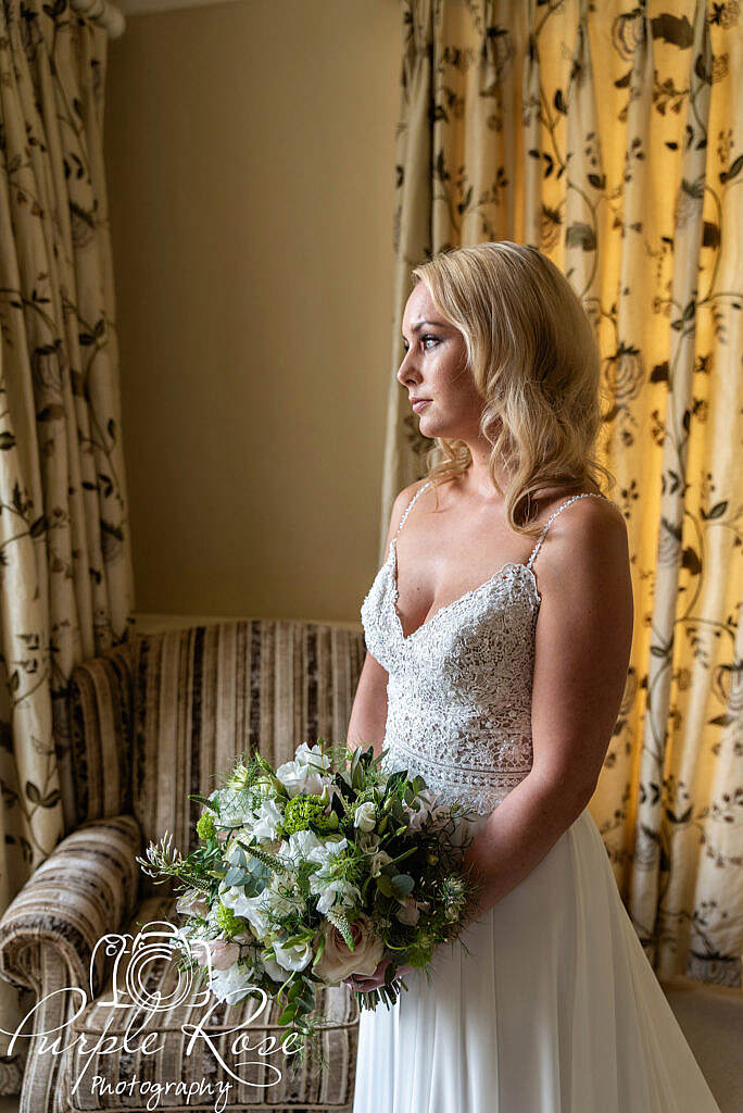 Bride holding her bouquet and looking out the iwndow