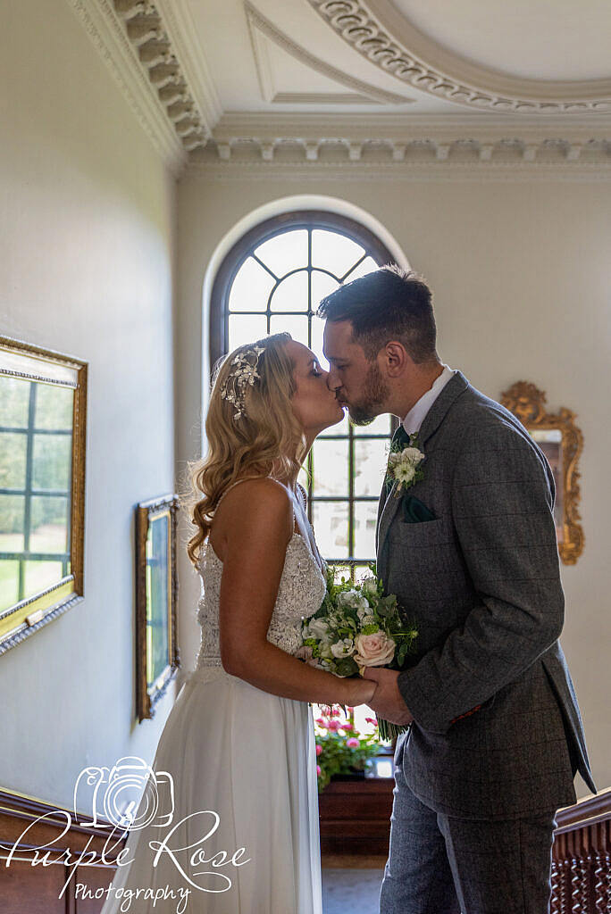 Bride and groom kissing in front of a window