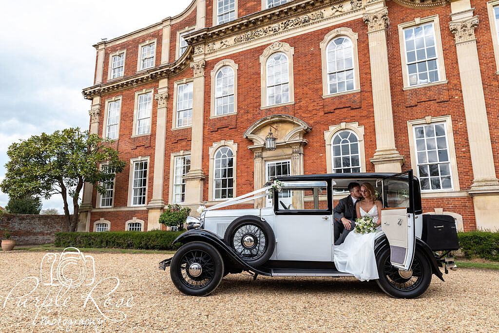 Bride and groom sat in their wedding car in front of their venue