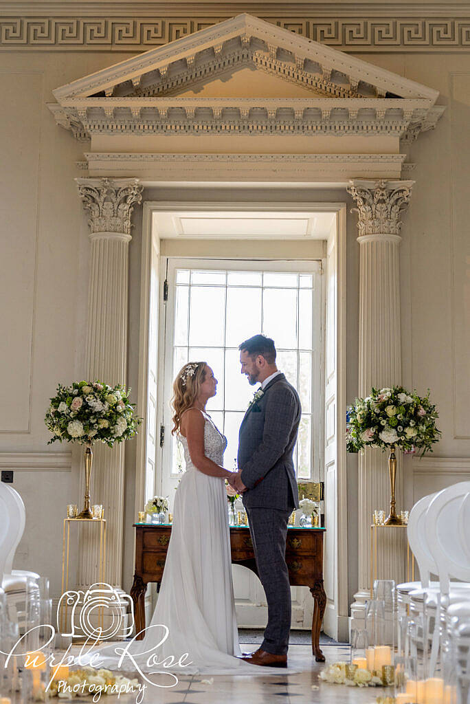 Bride and groom standing together in front of a large window