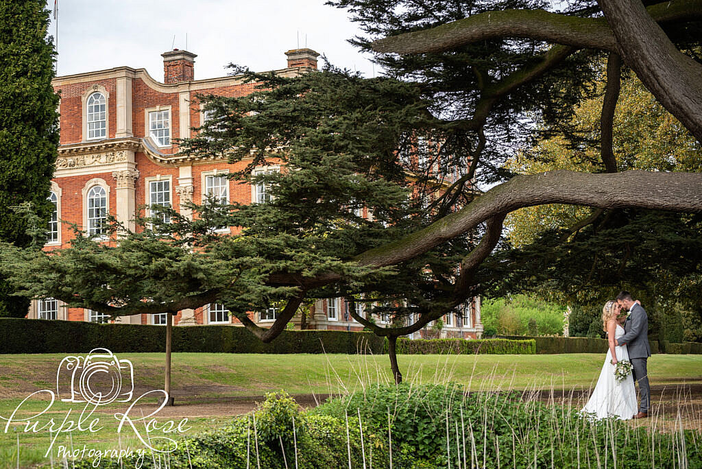 Bride and groom under a tree with Chicheley Hall in the background