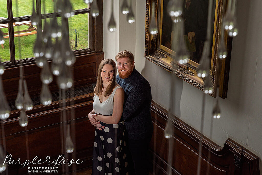 Couple standing by a window taken through a chandelier