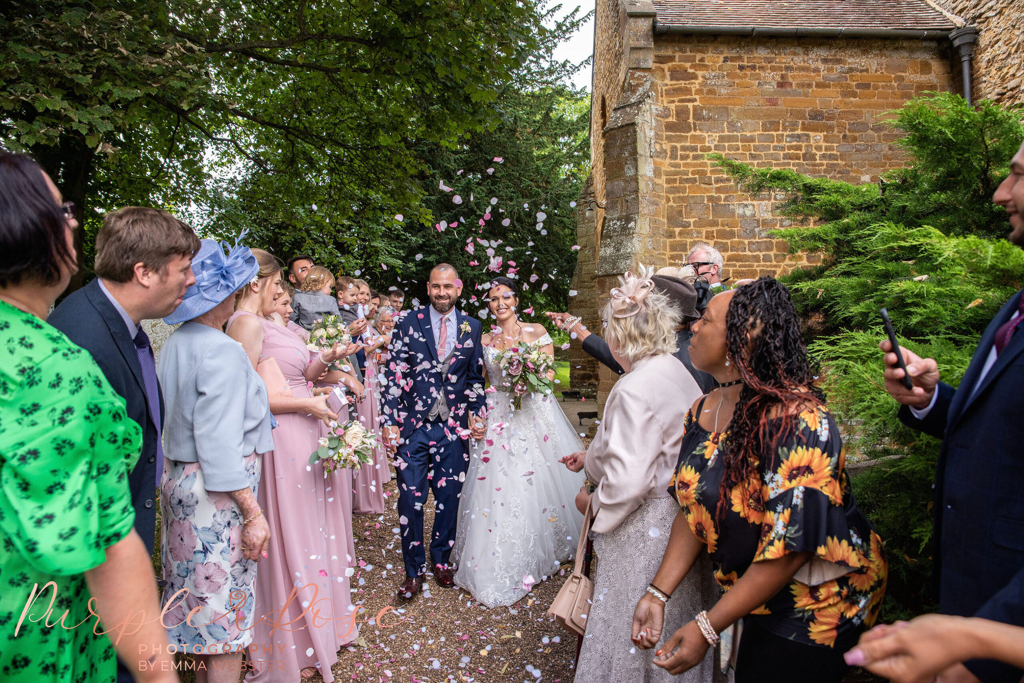 Wedding photo of a ride and groom leaving the church as guests throw confetti on their wedding day in Northampton