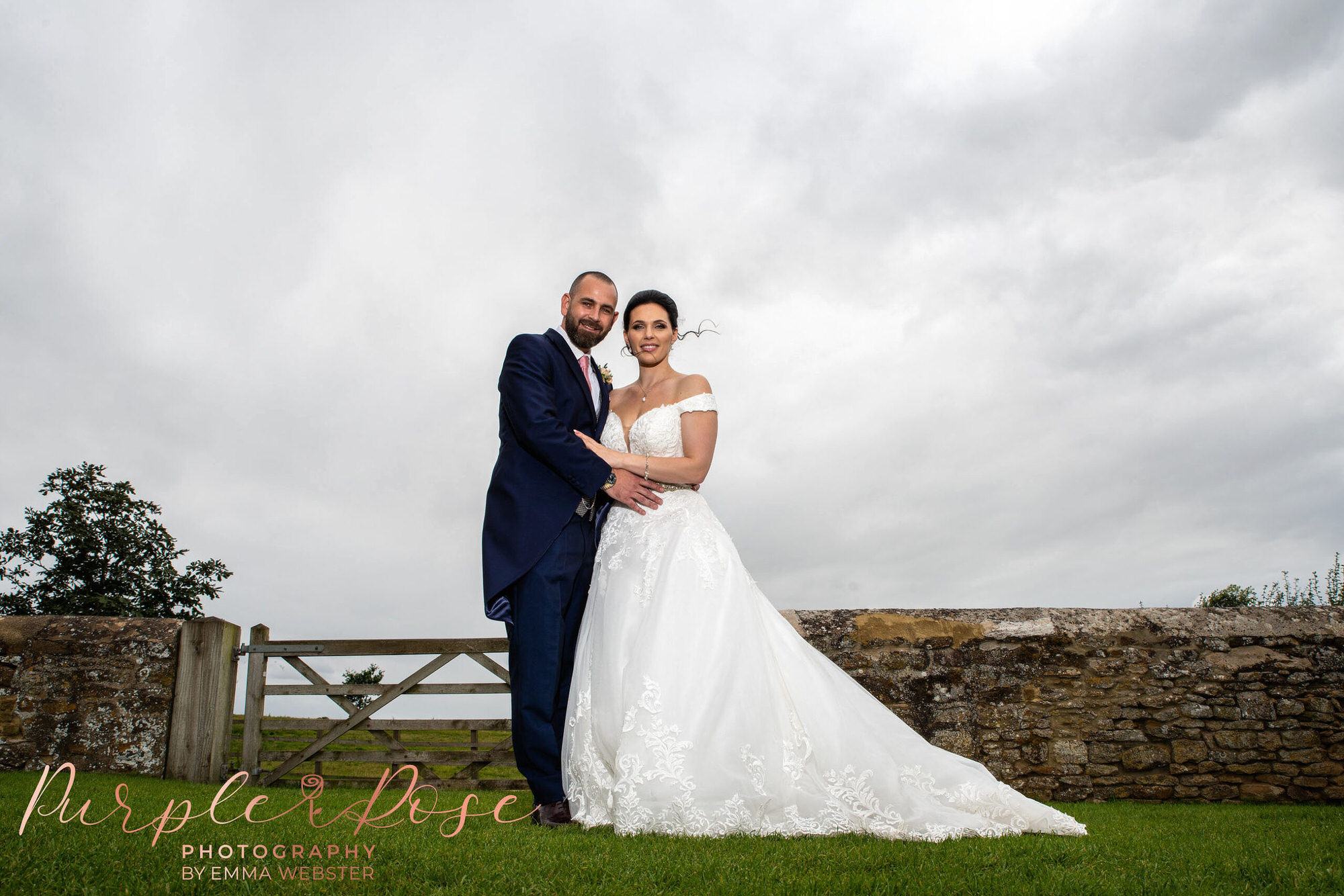 Bride and groom stood by gate and wall