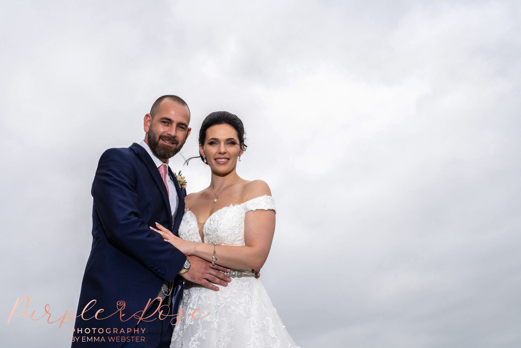 Bride and groom stood in front of a cloudy sky
