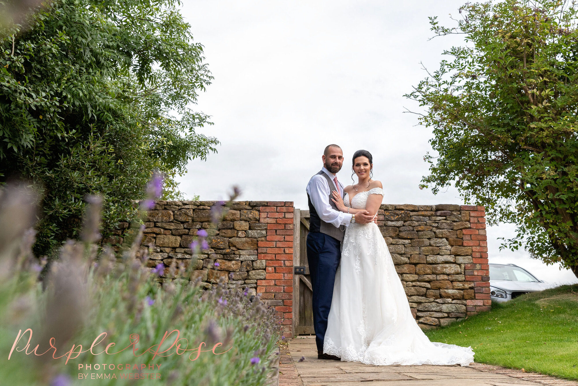 Bride and groom stood by lavender in a garden
