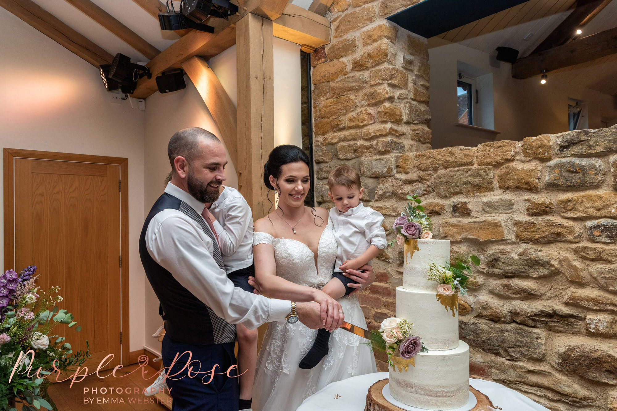 Bride, groom and their children cutting wedding cake