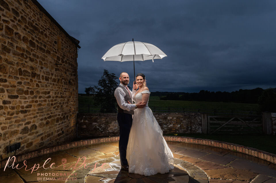 Night time photo of bride and groom under an umbrella