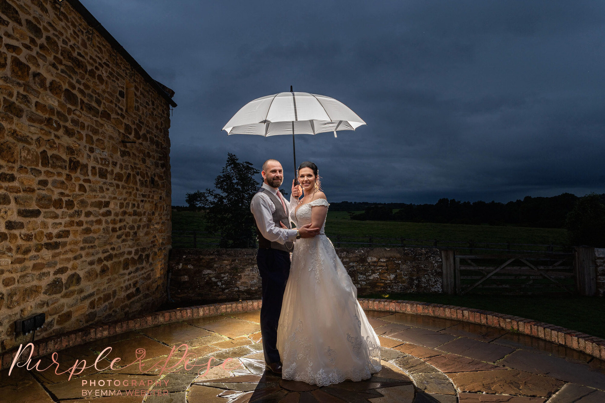 Night time photo of bride and groom under an umbrella at their wedding in Northampton