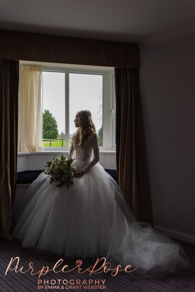 Photo of a bride sat looking out of a window on her wedding day in Milton Keynes
