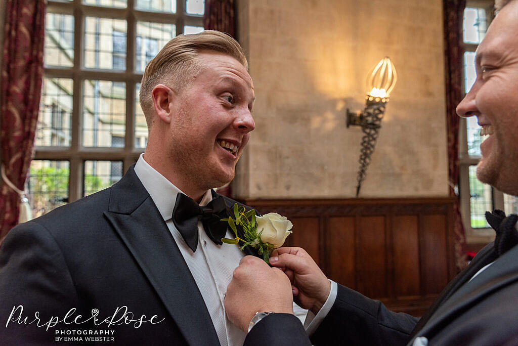 Groom laughing as hid buttonhole is attached