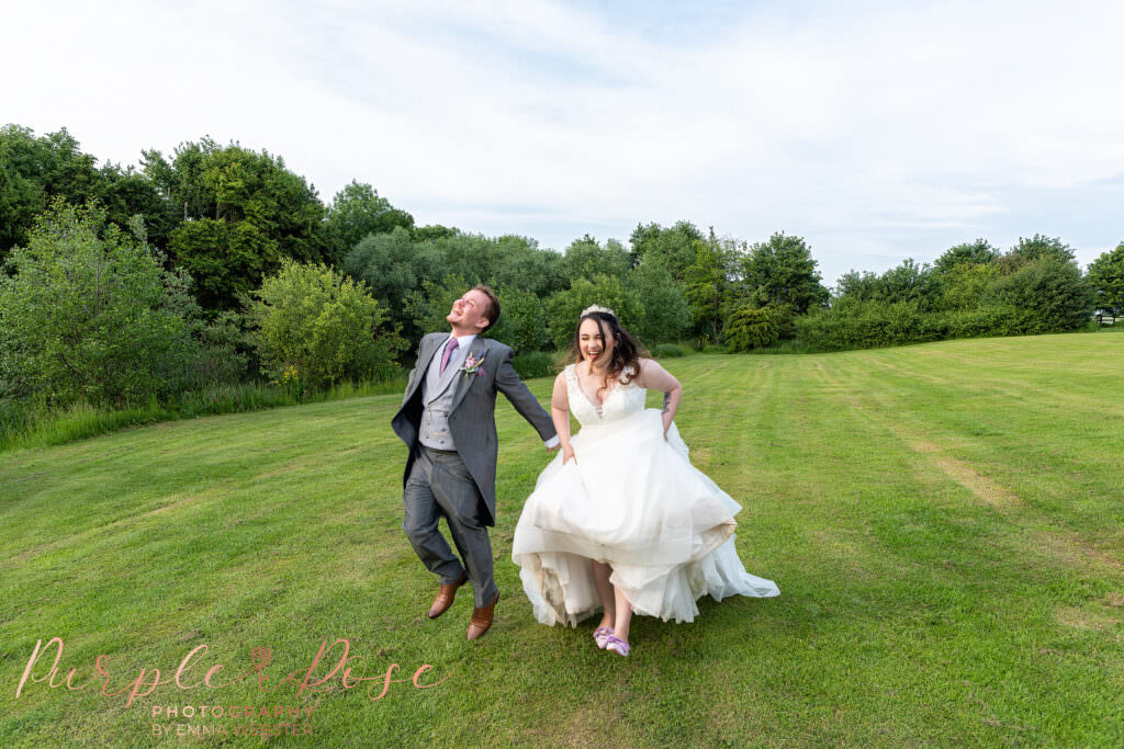 Bride and groom laughing as they skip through manicured lawn on their wedding day in Milton Keynes