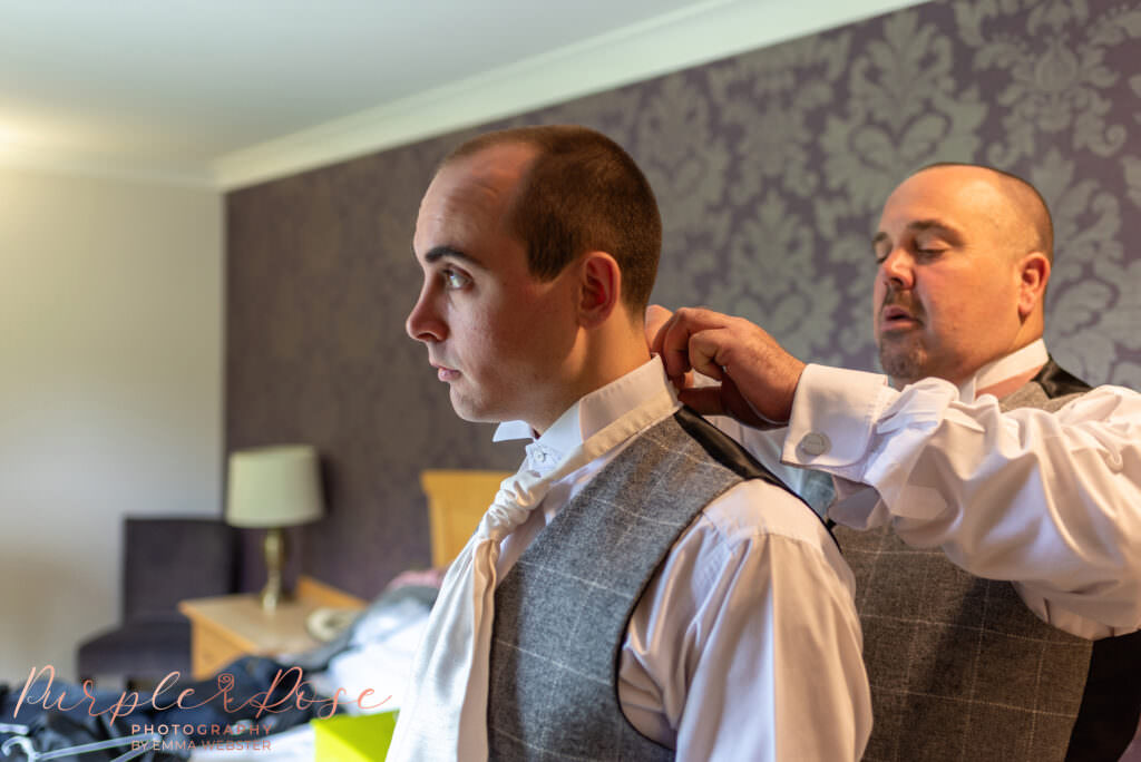 Best man helping groom adjust his collar