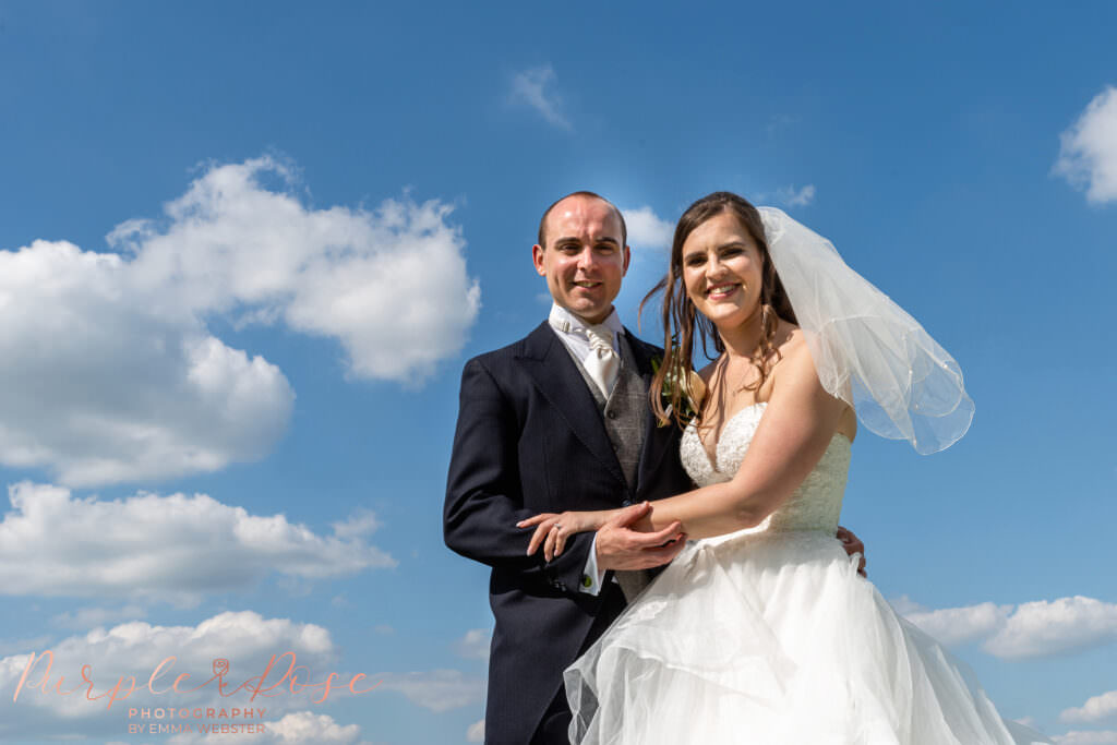 Bride and groom framed by blue sky and scattered clouds