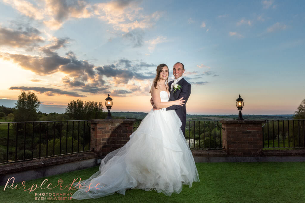 Bride and groom in front of a sunset on a balcony