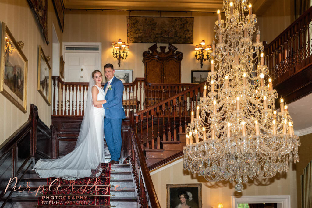 Bride and groom on staircase next to large chandelier