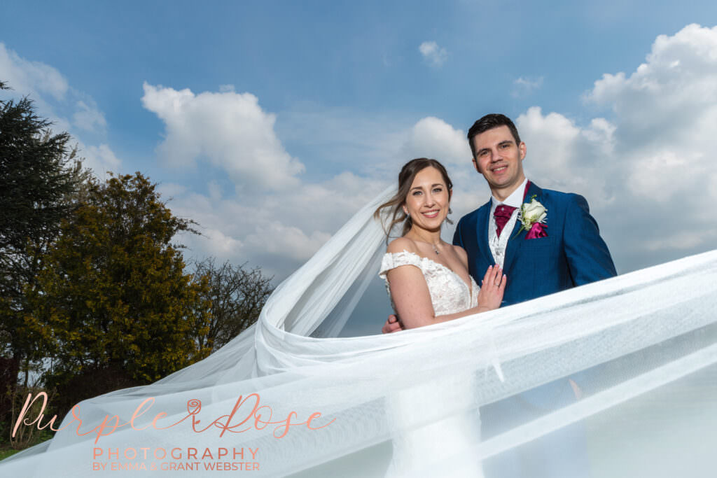 Photo of bride and groom on their wedding day with brides wedding veil swirling around them at theri wedding in Milton Keynes