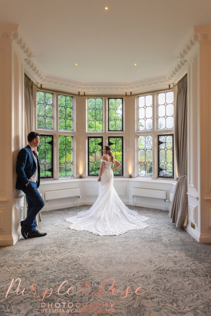 Photo of bride and groom stood in a bay window on their wedding day in Milton Keynes