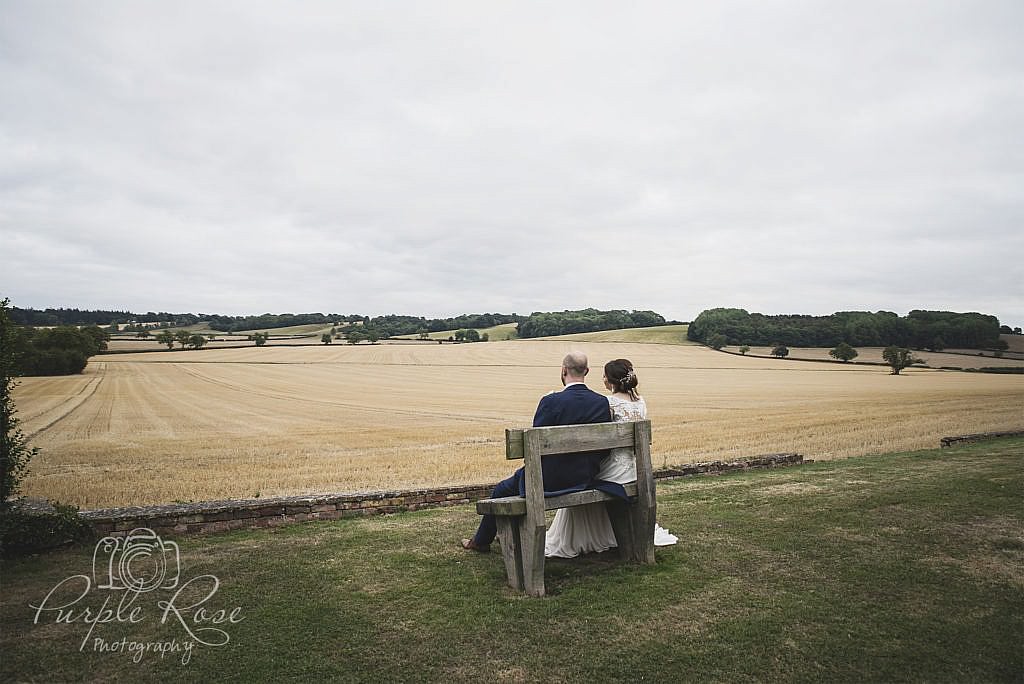 Bride and groom sat on bench looking out to open field