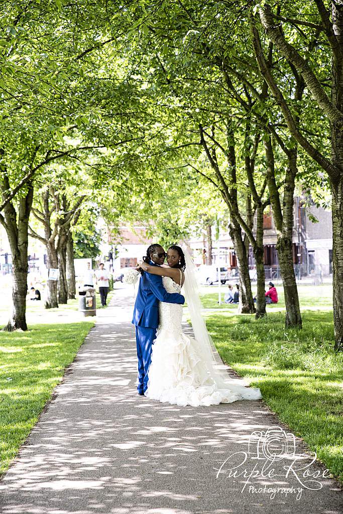 Bride and groom embracing in front of a tree lined pathway 