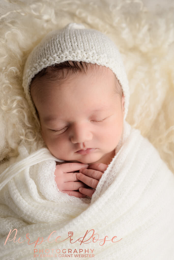 Photo of a newborn baby in a cream wrap and hat at his photoshoot in Milton Keynes