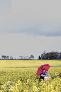 Bride and groom standing in a field with a red umbrella