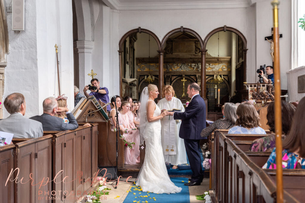 Photograph of a bride placing wedding ring on her husband in a church in Milton Keynes