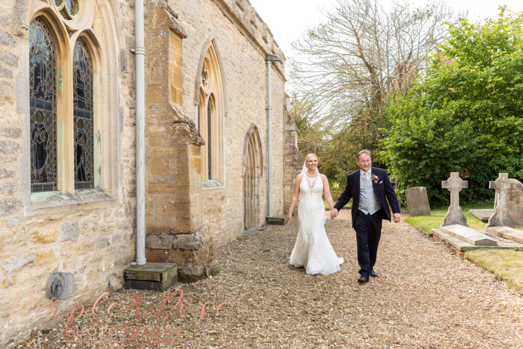 bride and groom walking alongside Chicheley Church  in Milton Keynes