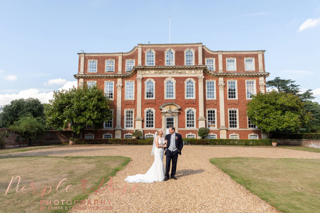 Photograph of a bride and groom stood in front of a manor house on their wedding day in Milton Keynes
