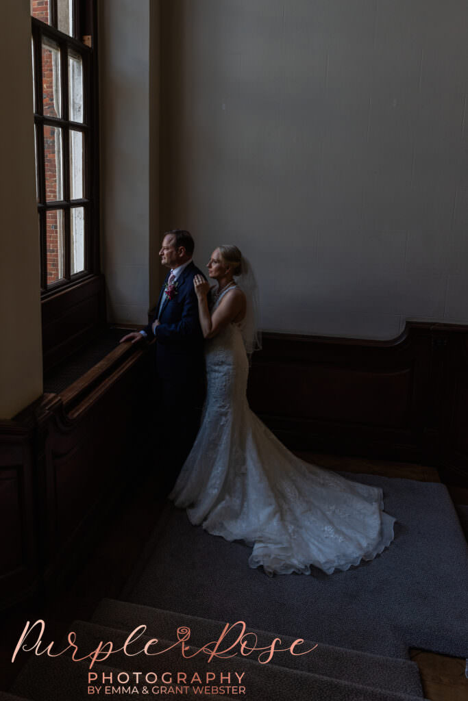 Photograph of a bride and groom on their wedding day in Milton Keynes stood by a tall window  in Milton Keynes