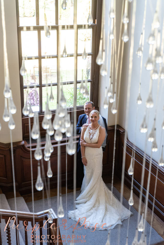 Photoshoot with a bride and groom on their wedding day in Milton Keynes, taken through a chandelier on a staircase in Milton Keynes