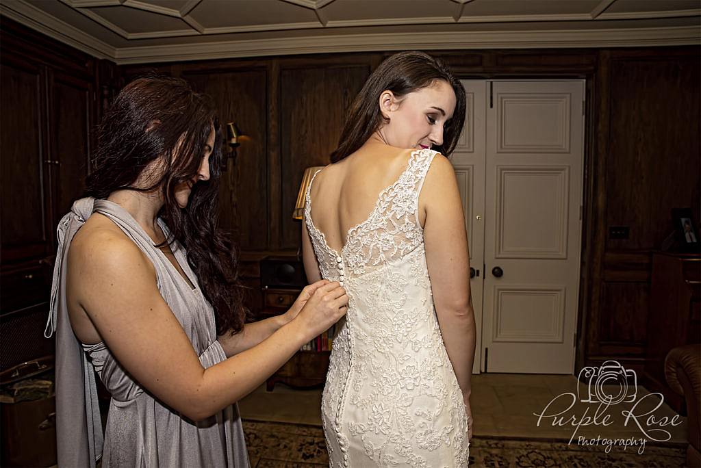 Bridesmaid buttoning up brides dress