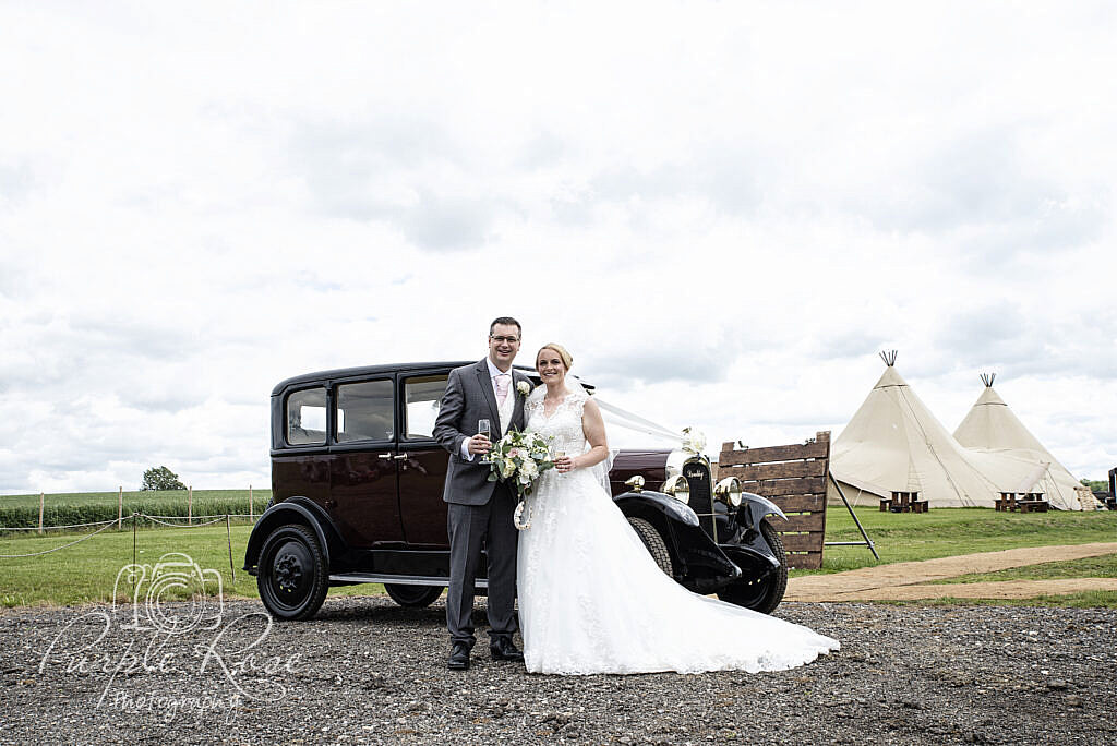Bride and groom in front of their car and reception venue