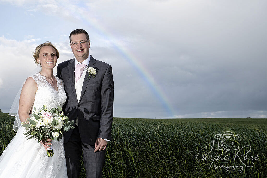 Bride and groom standing in front of a rainbow