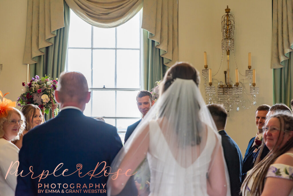 Photo of groom smiling as his bride arrives for the wedding ceremony