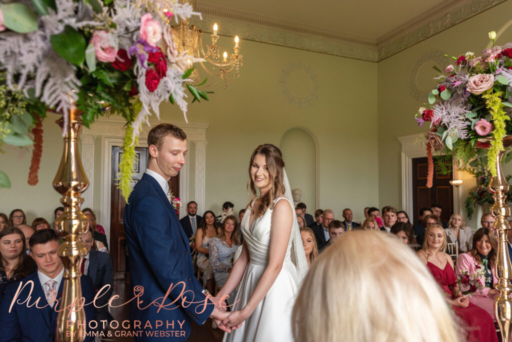 Photo of bride and groom smiling hand in hand during their wedding ceremony in Milton Keynes