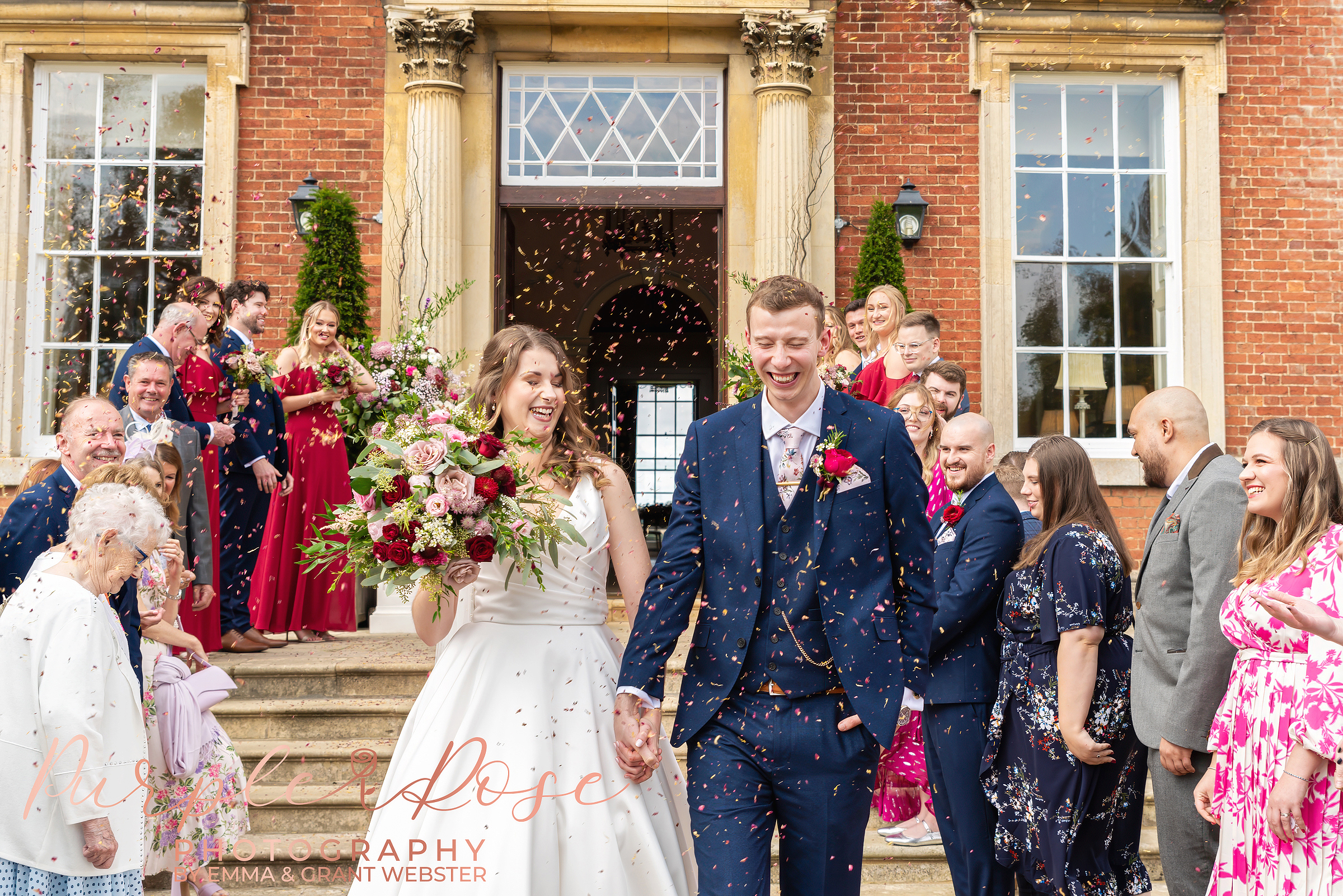 Photo of bride and groom laughing as their wedding guests throw confetti on their wedding day in Milton Keynes