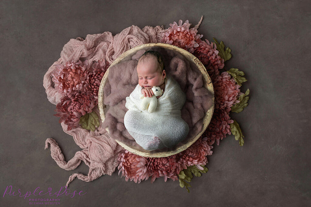 Newborn baby sleeping in bowl surrounded by flowers