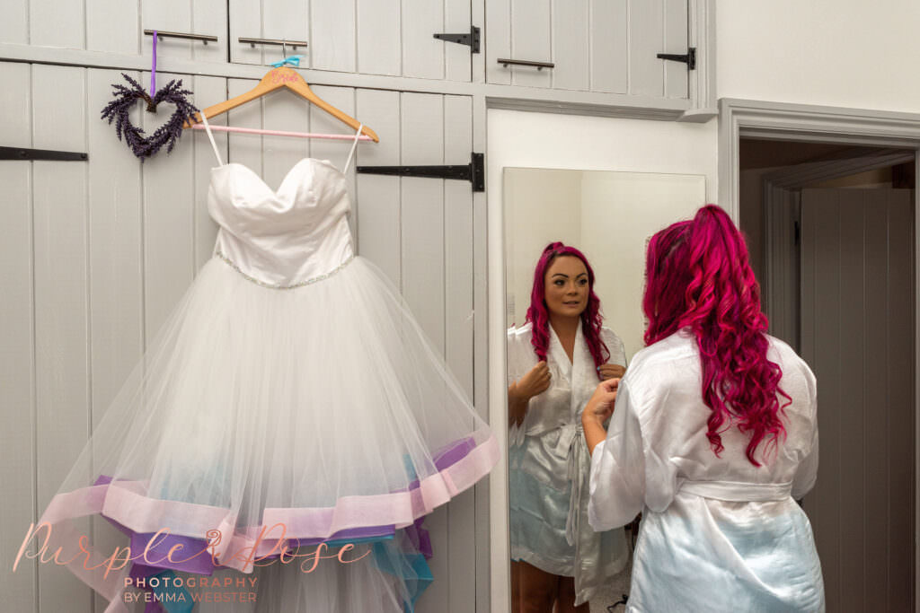 Bride looking in mirror stood next to her wedding dress