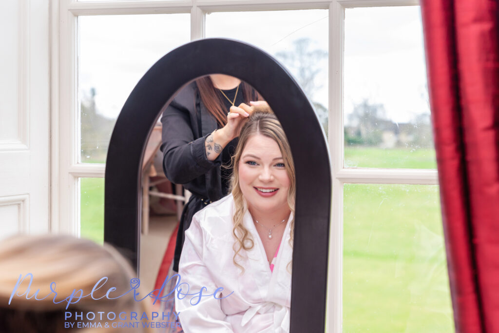 Photo fo abride smiling at her reflection in a mirrow as she gets ready for her wedding day in Milton Keynes
