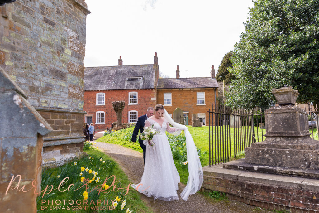 Photo of bride holding her wedding veil as she walks to the church for her wedding ceremony in Milton Keynes