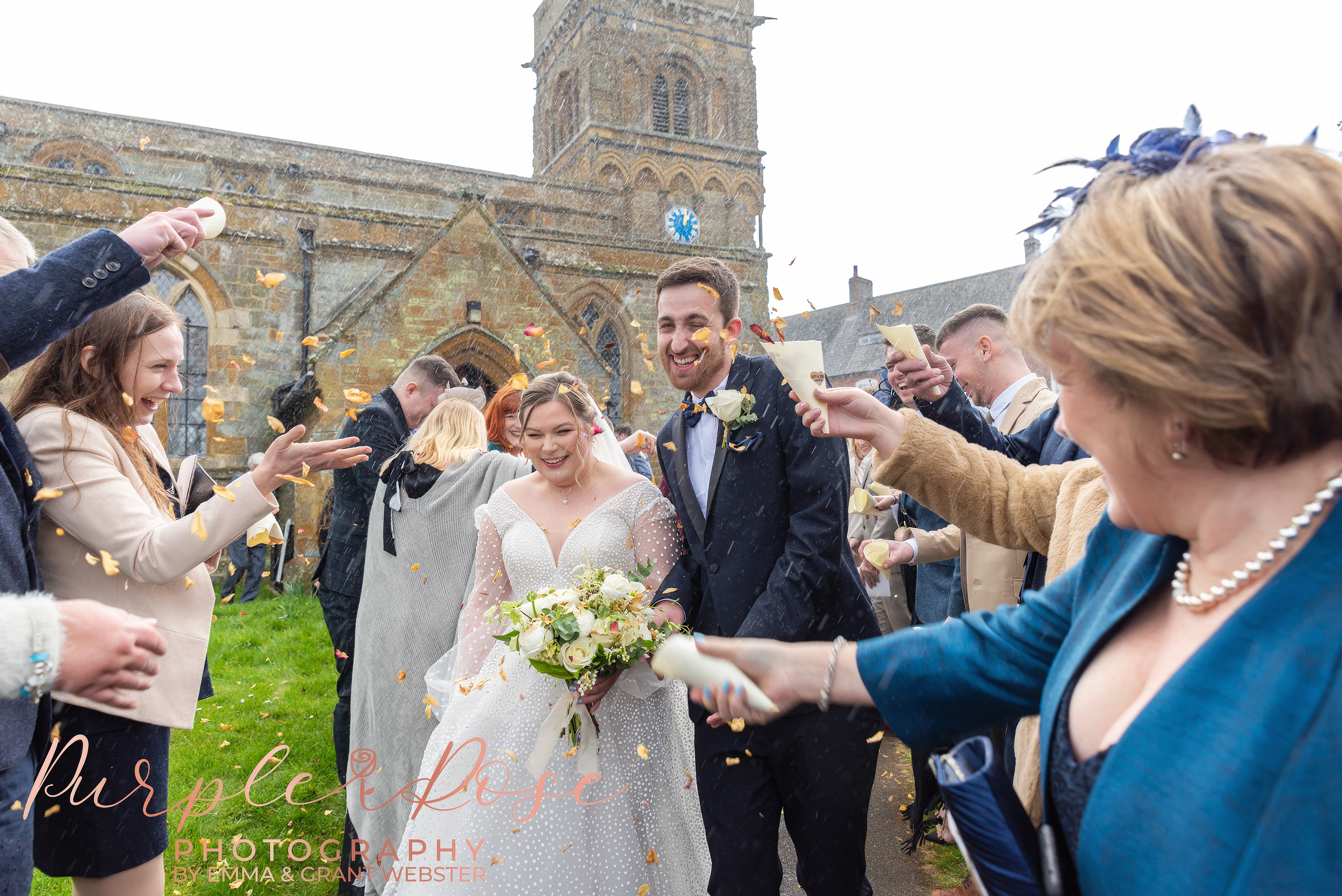 Photo of bride and groom haveing confetti thrown at them in the rain in Milton Keynes