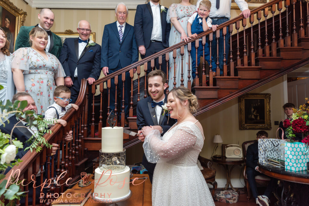 Photo of bride and groom being watched by wedding guests as they cut their wedding cake in Milton Keynes
