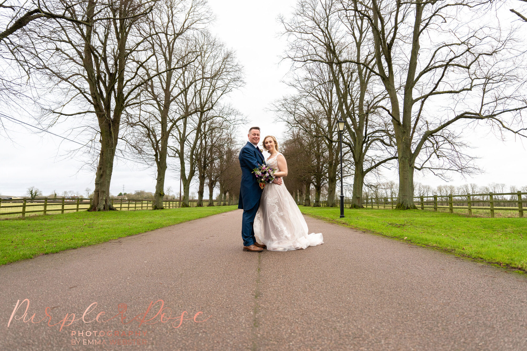 Bride and groom stood on tree lined driveway