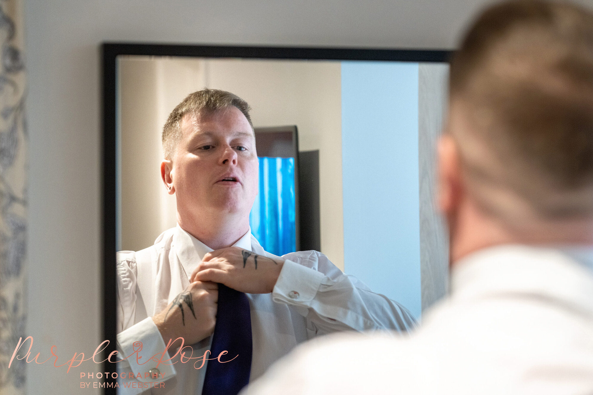 Groom adjusting his tie in the mirror